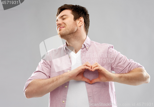 Image of man making hand heart gesture over grey background