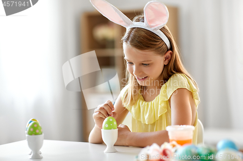 Image of happy girl coloring easter egg at home