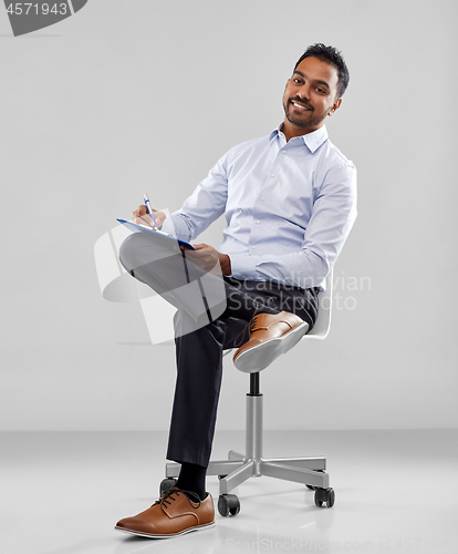 Image of smiling indian businessman writing to clipboard