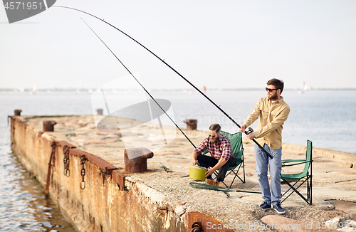 Image of happy friends with fishing rods on pier