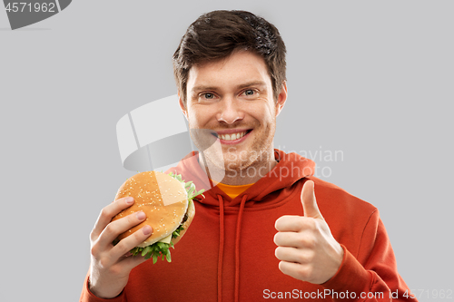 Image of happy young man with hamburger showing thumbs up