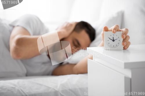 Image of close up of man in bed reaching for alarm clock