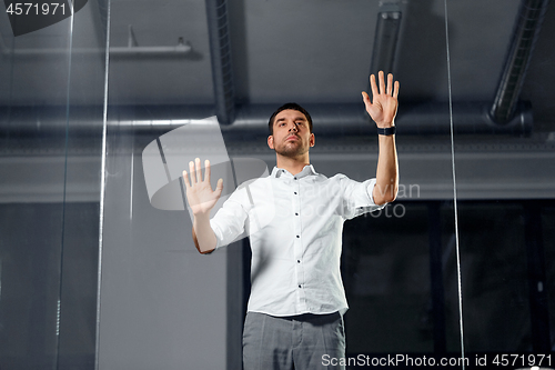Image of businessman touching glass wall at night office