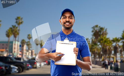 Image of happy indian delivery man with clipboard in blue