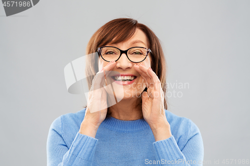 Image of senior woman in glasses calling over grey