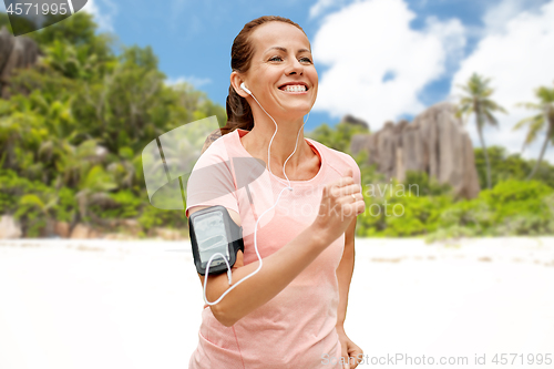 Image of woman with earphones and armband running on beach