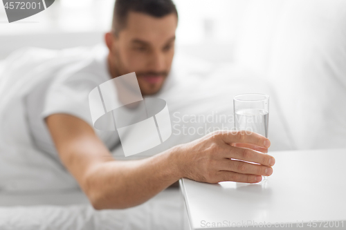 Image of close up of man in bed reaching to glass of water