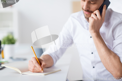 Image of businessman calling on cell writing to notebook