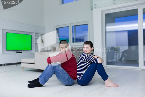 Image of young couple sitting with back to each other on floor