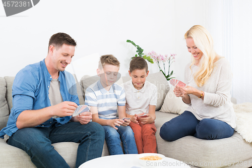 Image of Happy young family playing card game at home.