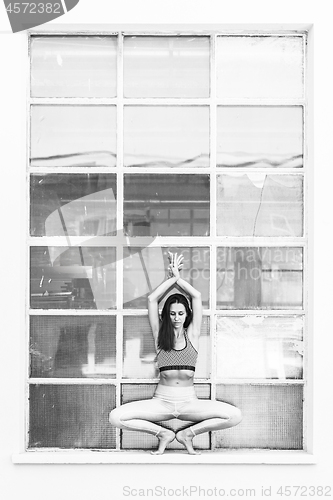 Image of Fit sporty active girl in fashion sportswear doing yoga fitness exercise in front of big industrial window frame. colorful reflections in window glass. Urban style yoga. Black and white