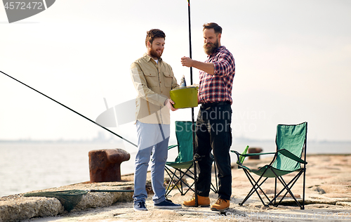 Image of happy friends with fish and fishing rods on pier