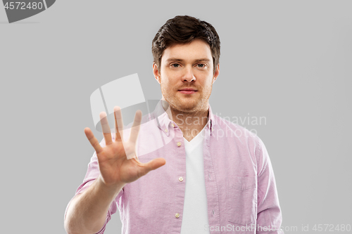 Image of young man showing five fingers over grey