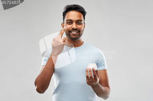 Image of happy indian man applying cream to face