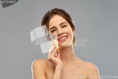 Image of young woman cleaning face with exfoliating sponge