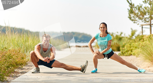 Image of smiling couple stretching legs on beach