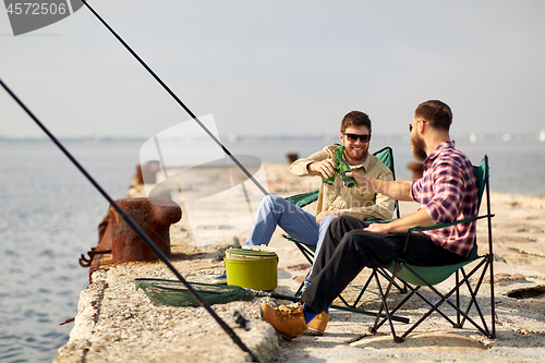 Image of happy friends fishing and drinking beer on pier