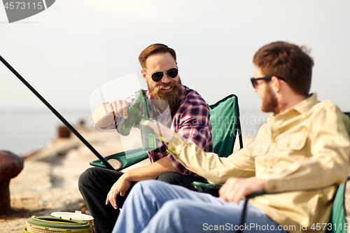 Image of happy friends fishing and drinking beer on pier