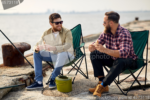 Image of happy friends fishing and eating sandwiches