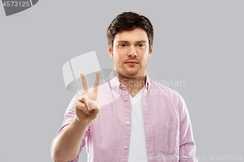 Image of young man showing two fingers over grey background