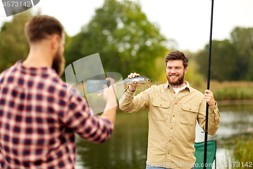 Image of friend photographing fisherman with fish at lake