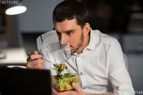 Image of businessman with computer eating at night office