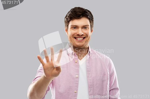 Image of young man showing four fingers over grey