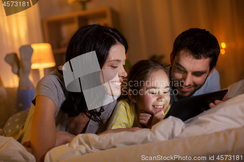 Image of family with tablet pc in bed at night at home