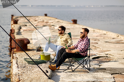 Image of happy friends fishing and drinking beer on pier