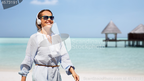 Image of woman with headphones walking along summer beach