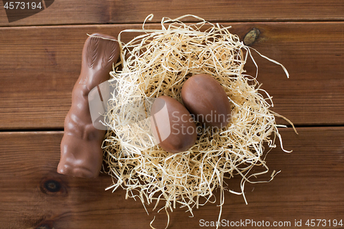 Image of chocolate bunny and eggs in straw nest on wood
