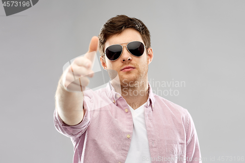 Image of young man in sunglasses making hand gun gesture