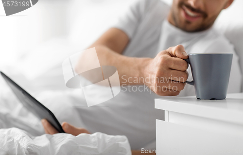 Image of man with tablet computer drinking coffee in bed