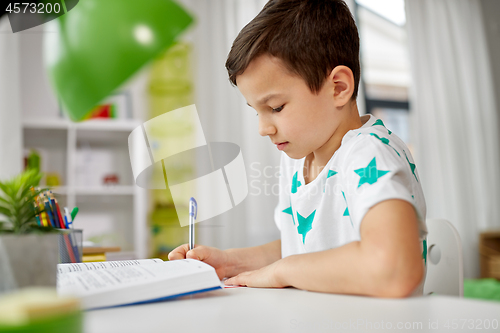 Image of student boy with book writing to notebook at home