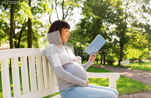 Image of happy pregnant asian woman reading book at park