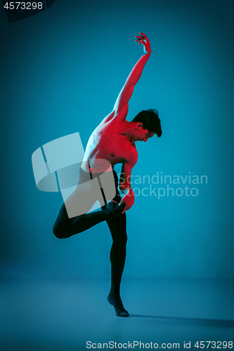 Image of The male athletic ballet dancer performing dance on blue background. Studio shot. Ballet concept. Fit young man. Caucasian model