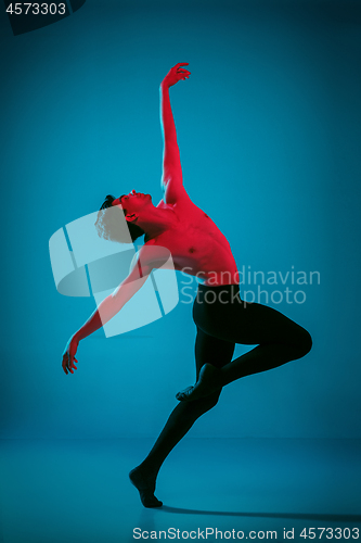 Image of The male athletic ballet dancer performing dance on blue background. Studio shot. Ballet concept. Fit young man. Caucasian model