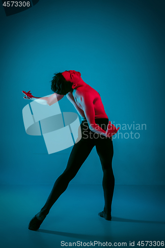 Image of The male athletic ballet dancer performing dance on blue background. Studio shot. Ballet concept. Fit young man. Caucasian model