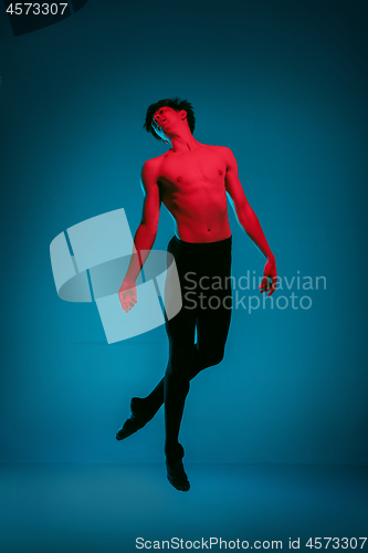 Image of The male athletic ballet dancer performing dance on blue background. Studio shot. Ballet concept. Fit young man. Caucasian model