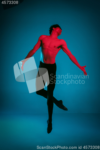 Image of The male athletic ballet dancer performing dance on blue background. Studio shot. Ballet concept. Fit young man. Caucasian model