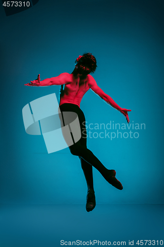 Image of The male athletic ballet dancer performing dance on blue background. Studio shot. Ballet concept. Fit young man. Caucasian model