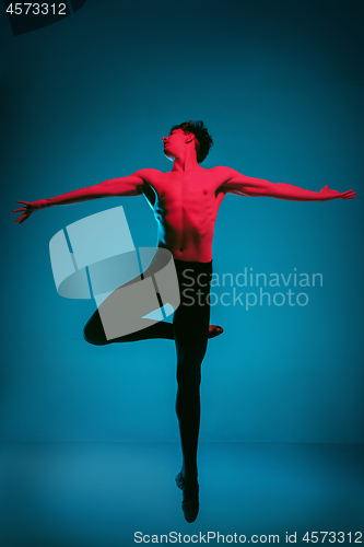 Image of The male athletic ballet dancer performing dance on blue background. Studio shot. Ballet concept. Fit young man. Caucasian model