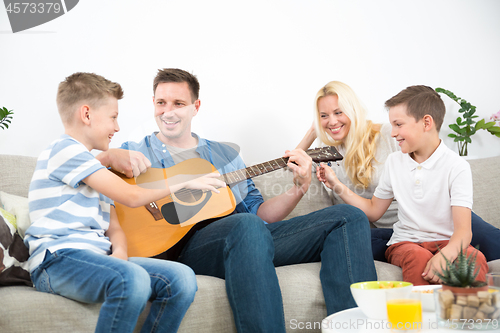 Image of Happy caucasian family smiling, playing guitar and singing songs together at cosy modern home