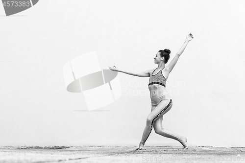 Image of Fit sporty active girl in fashion sportswear doing yoga fitness exercise in front of gray wall, outdoor sports, urban style. Black and white photo.