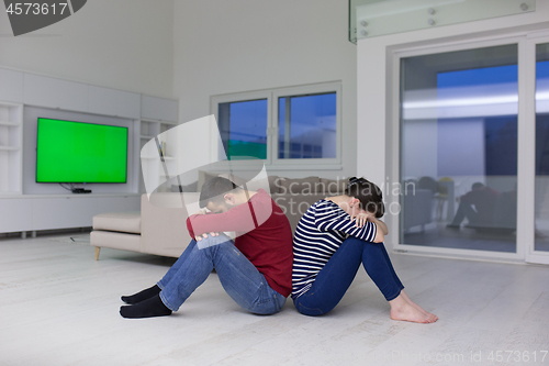 Image of young couple sitting with back to each other on floor