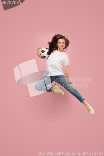 Image of Forward to the victory.The young woman as soccer football player jumping and kicking the ball at studio on pink