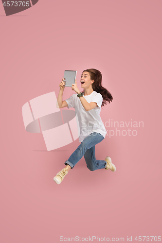 Image of Image of young woman over pink background using laptop computer or tablet gadget while jumping.