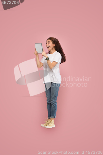 Image of Image of young woman over pink background using laptop computer or tablet gadget while jumping.