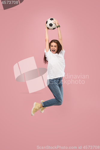 Image of Forward to the victory.The young woman as soccer football player jumping and kicking the ball at studio on pink