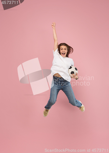 Image of Forward to the victory.The young woman as soccer football player jumping and kicking the ball at studio on pink